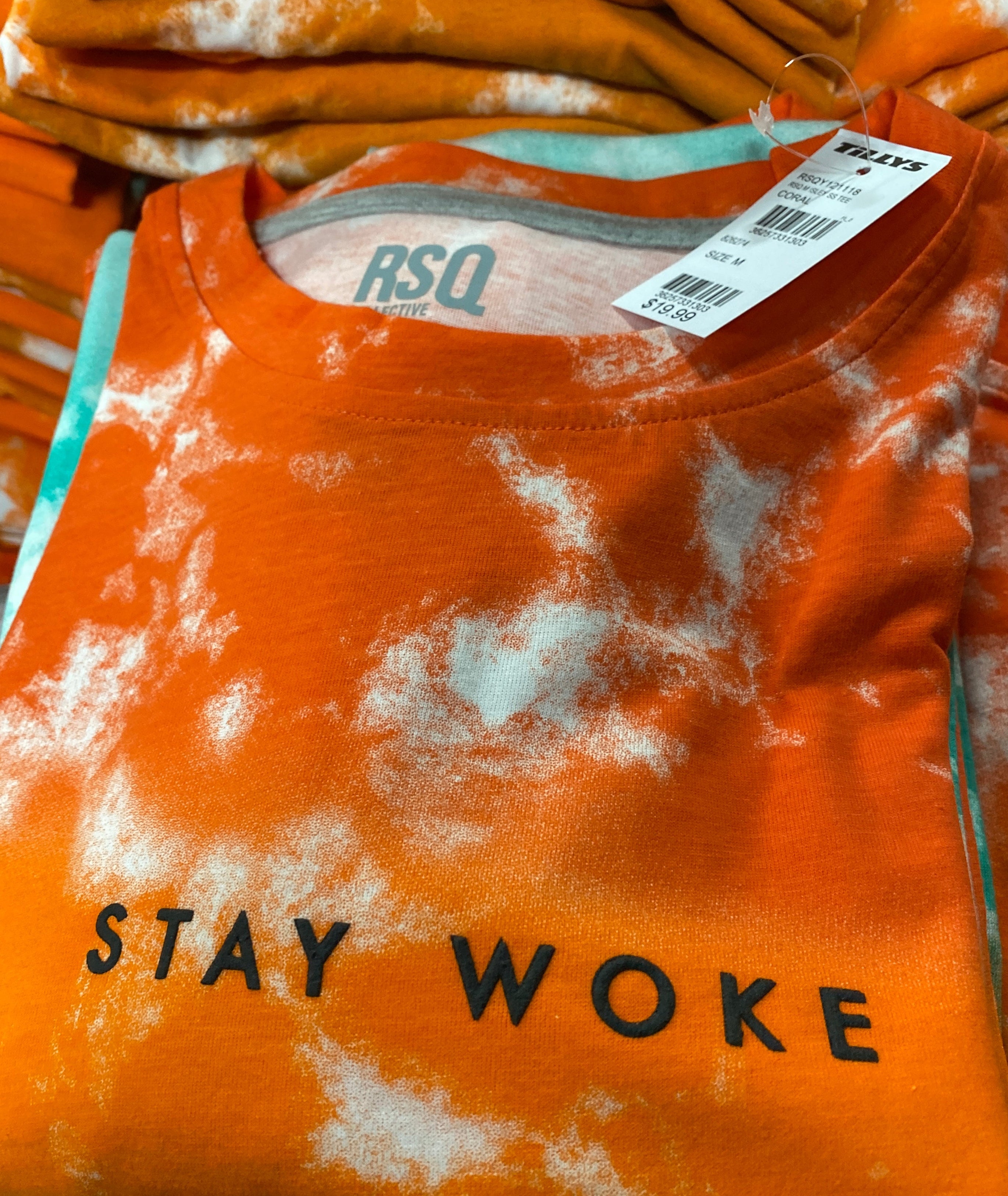 Orange t-shirt with 'STAY WOKE' text and tie-dye design, displayed with a tag.